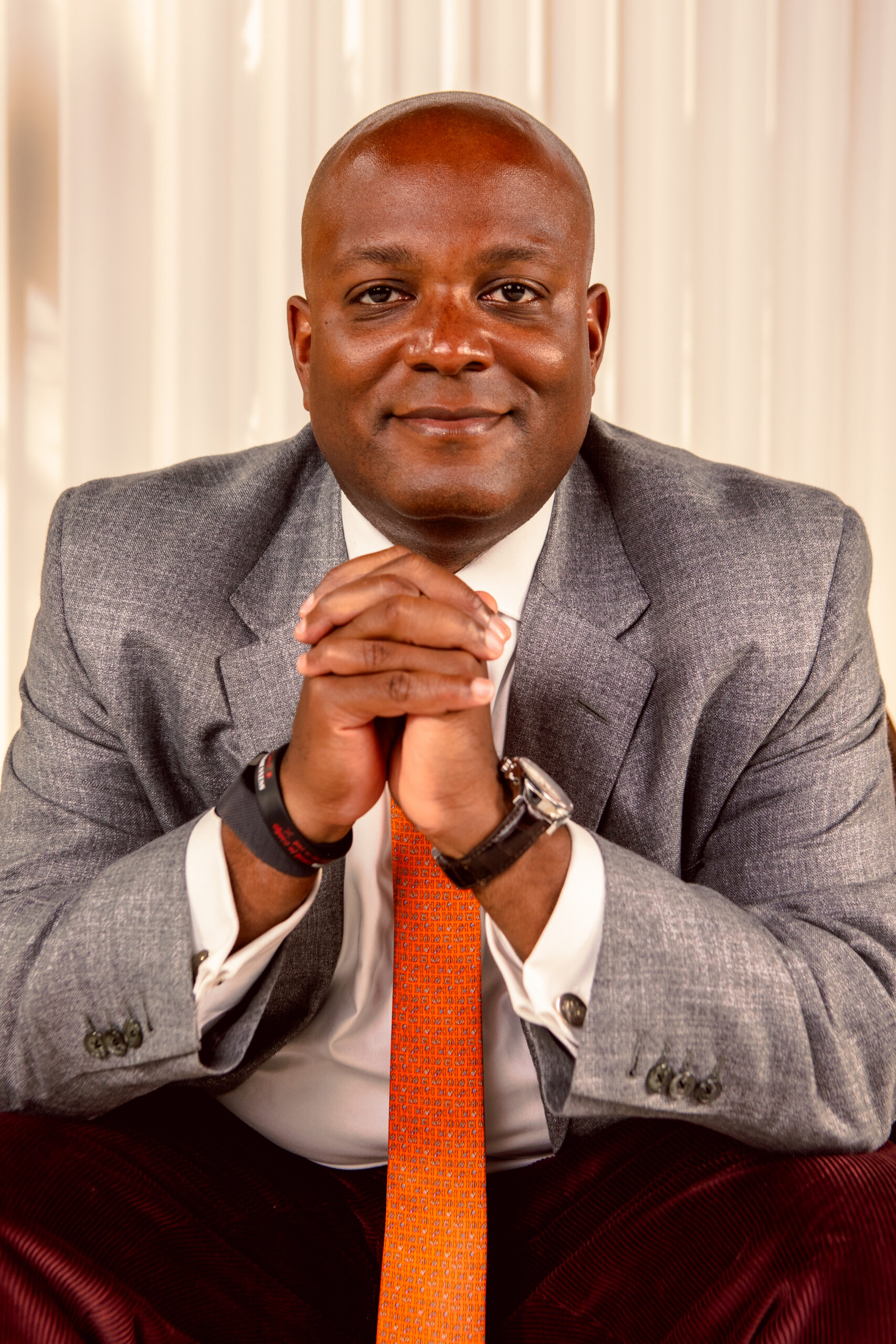 Joel Stone wearing a grey suite with a orange tie.