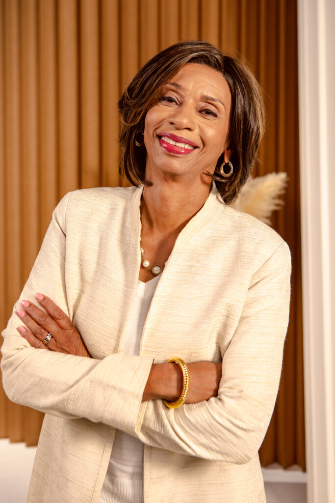 Black Woman Wearing a cream suite standing with her arms across her chest. 